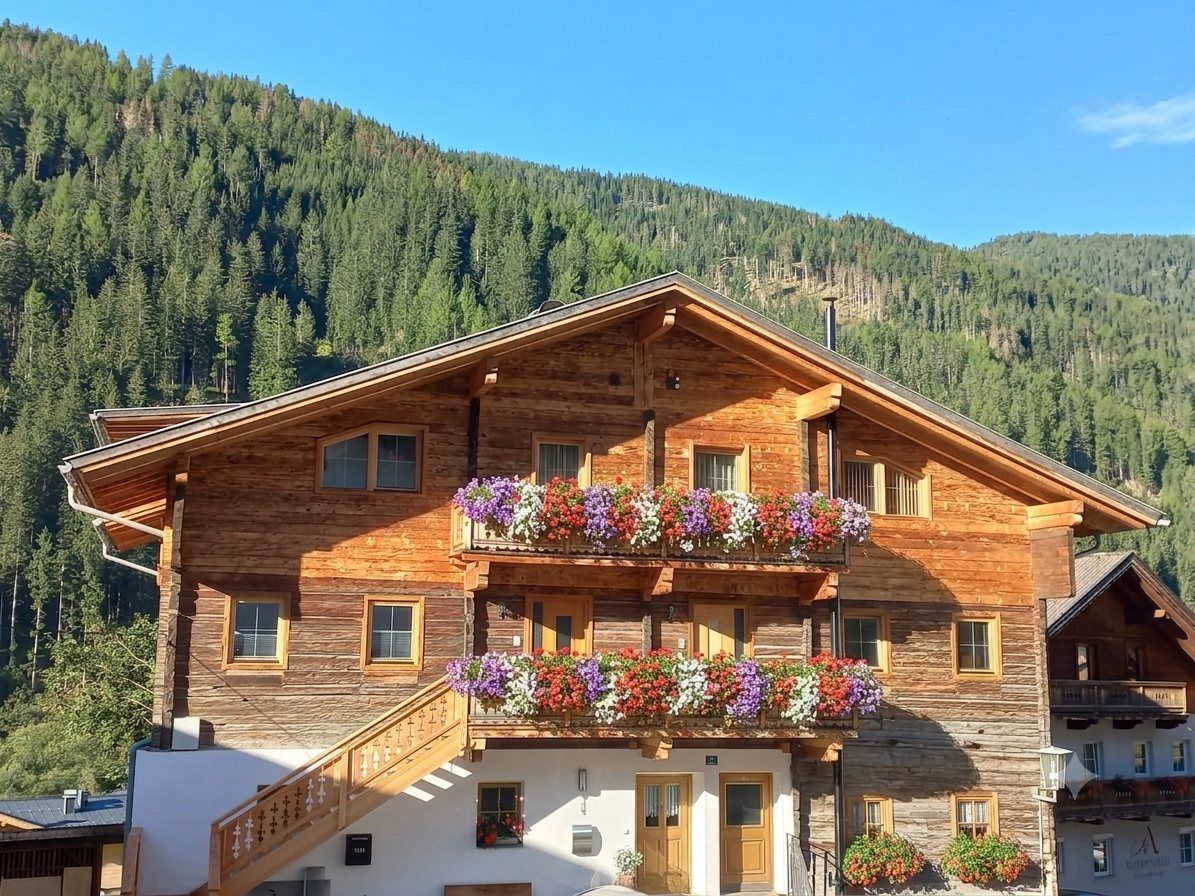 Appartements Höllhaus im Sommer mit blühenden Balkonen vor dem Bergwald